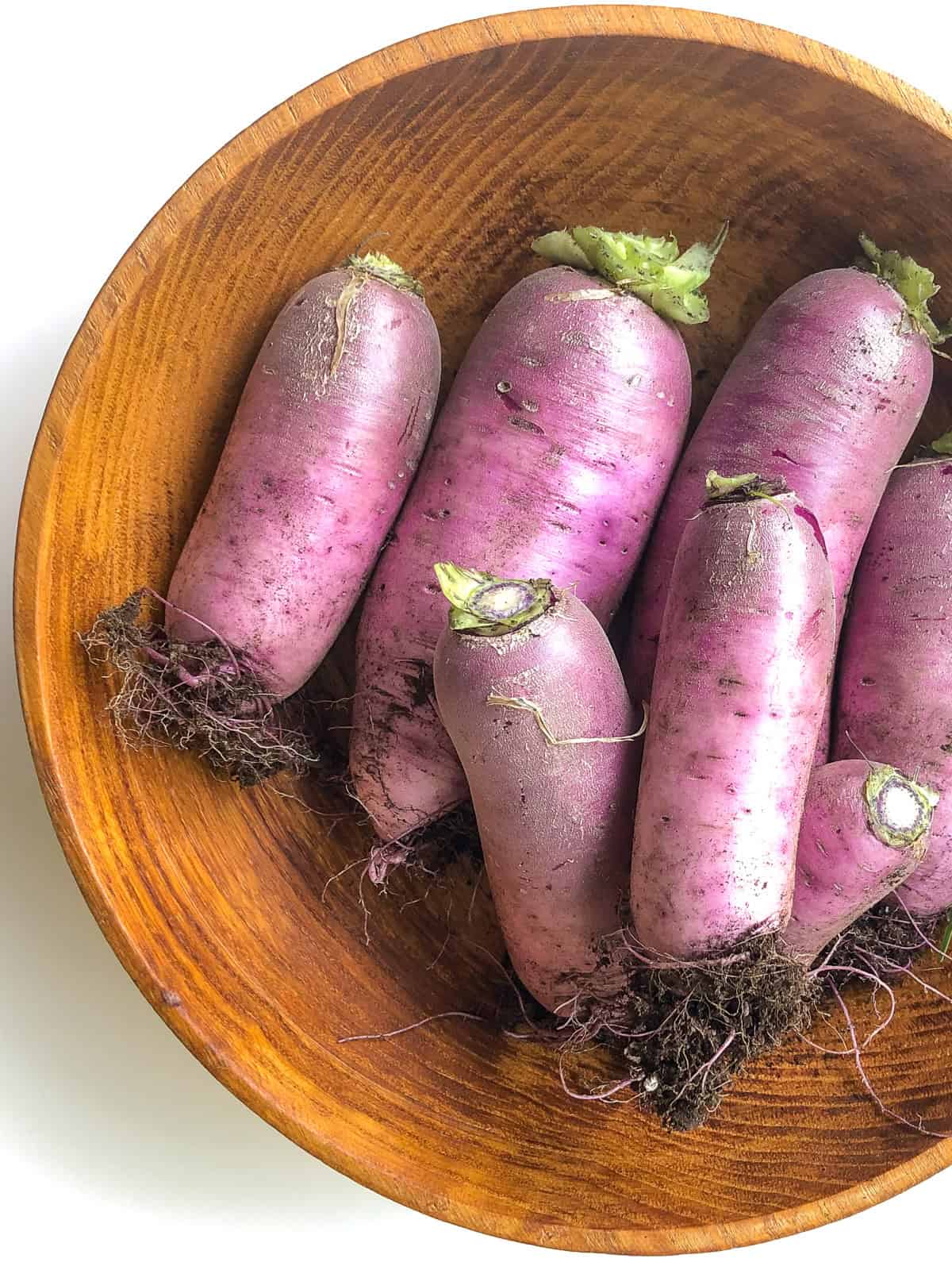 An image of a wooden bowl filled with freshly picked purple daikon radishes.