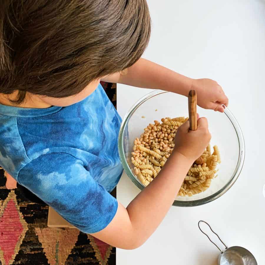 An image of a boy making pasta salad.