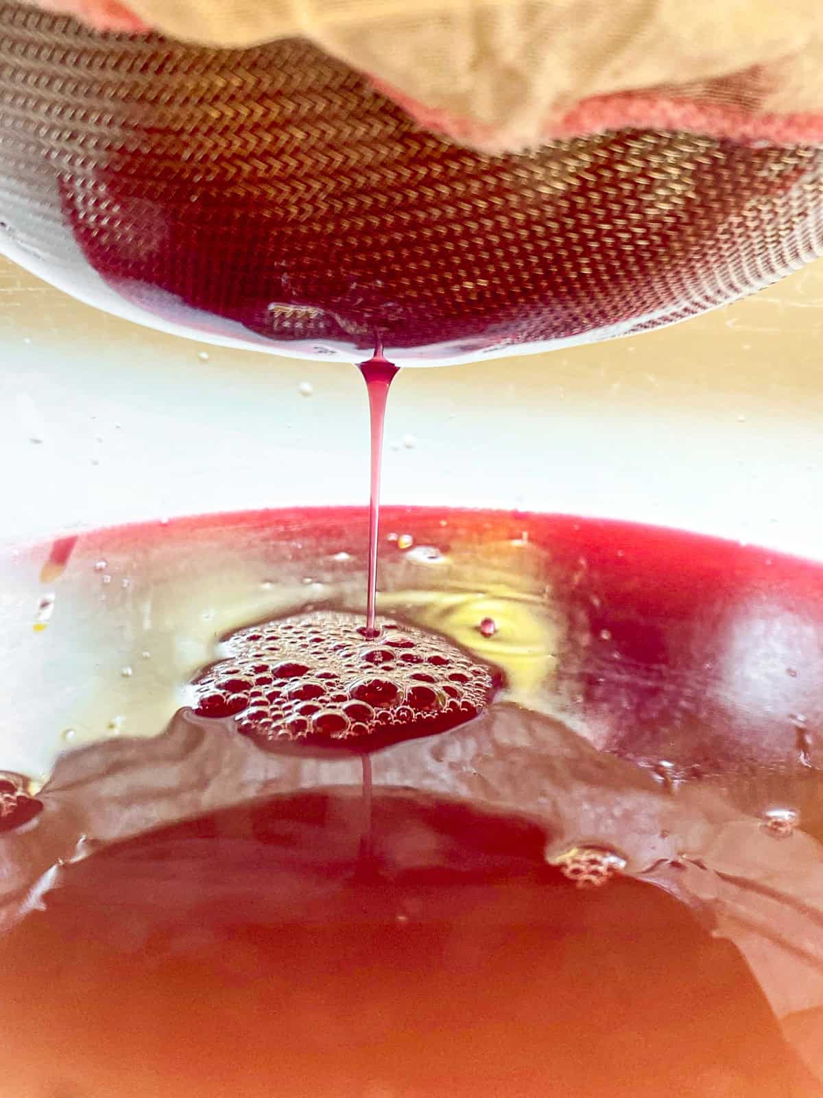 A close up image of cooked rhubarb being strained through cheesecloth and a mesh strainer over a glass bowl.