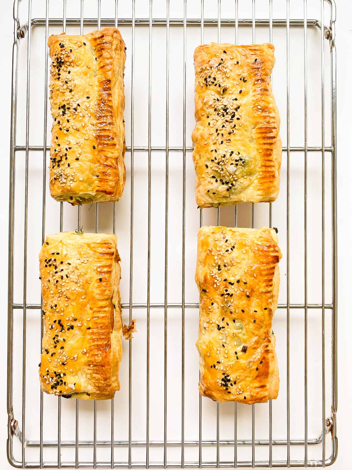 An image of flaky greens filled puff pastry roll on a silver metal baking rack.