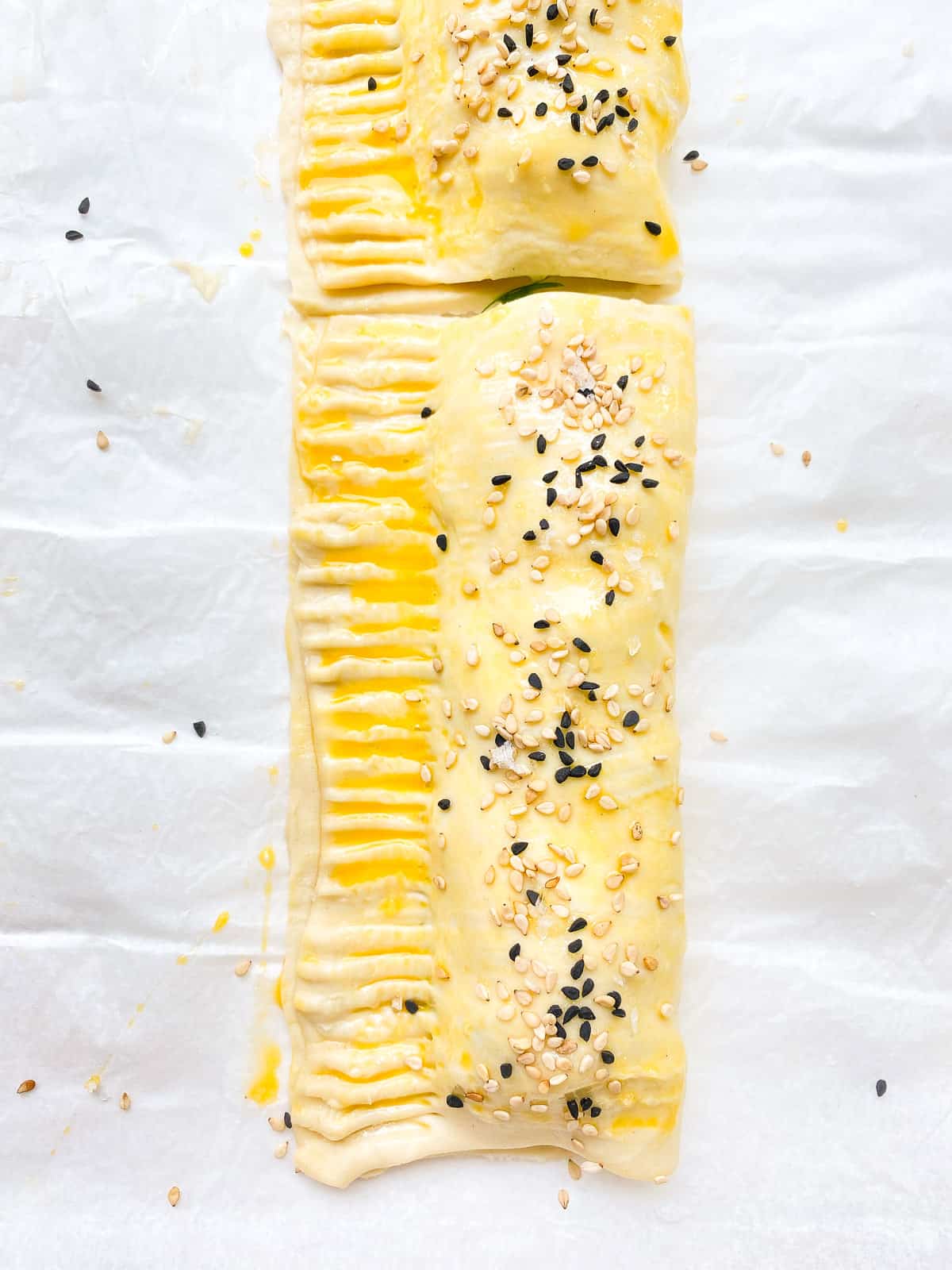 An image of a flaky greens filled sausage roll before being baked.