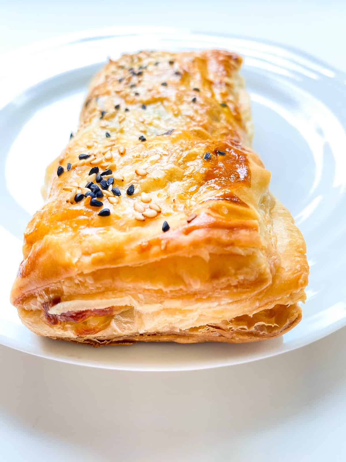 An image of a flaky greens filled puff pastry roll on a white ceramic plate.