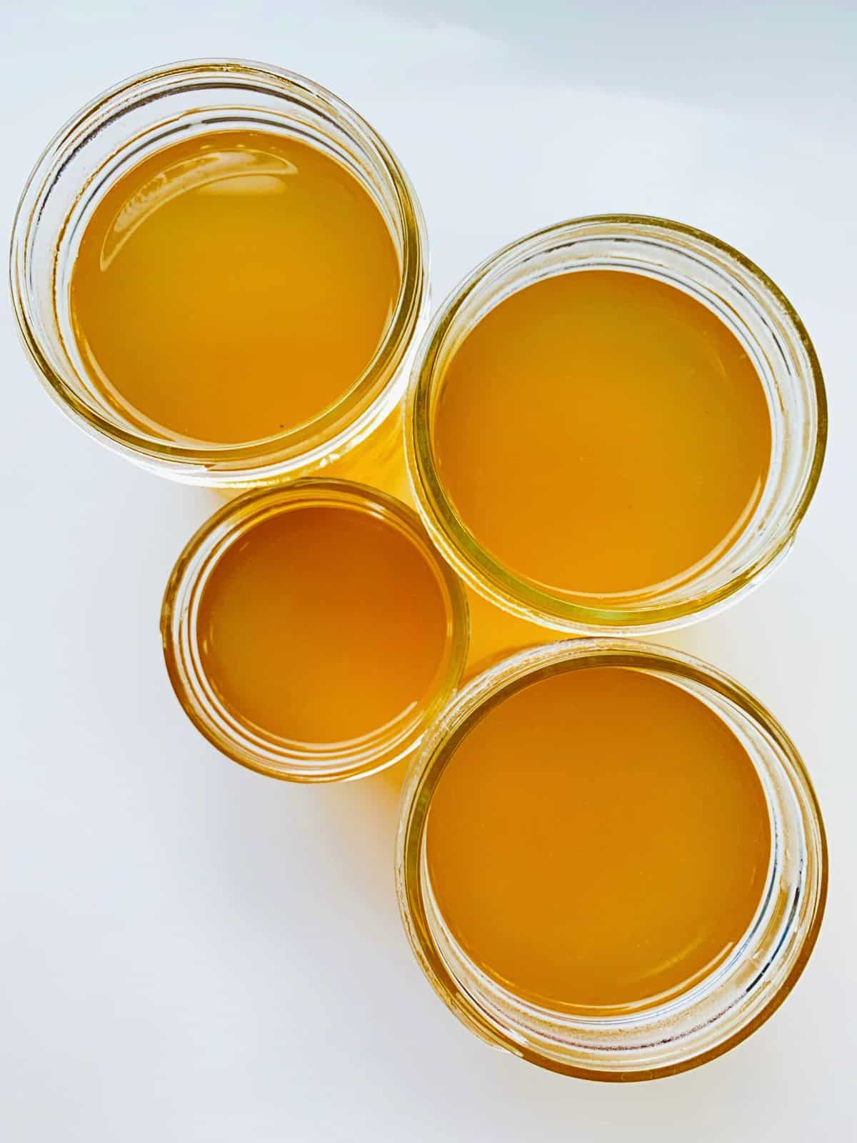 An image of four glass jars, as seen from above, filled with strained Corn Broth.