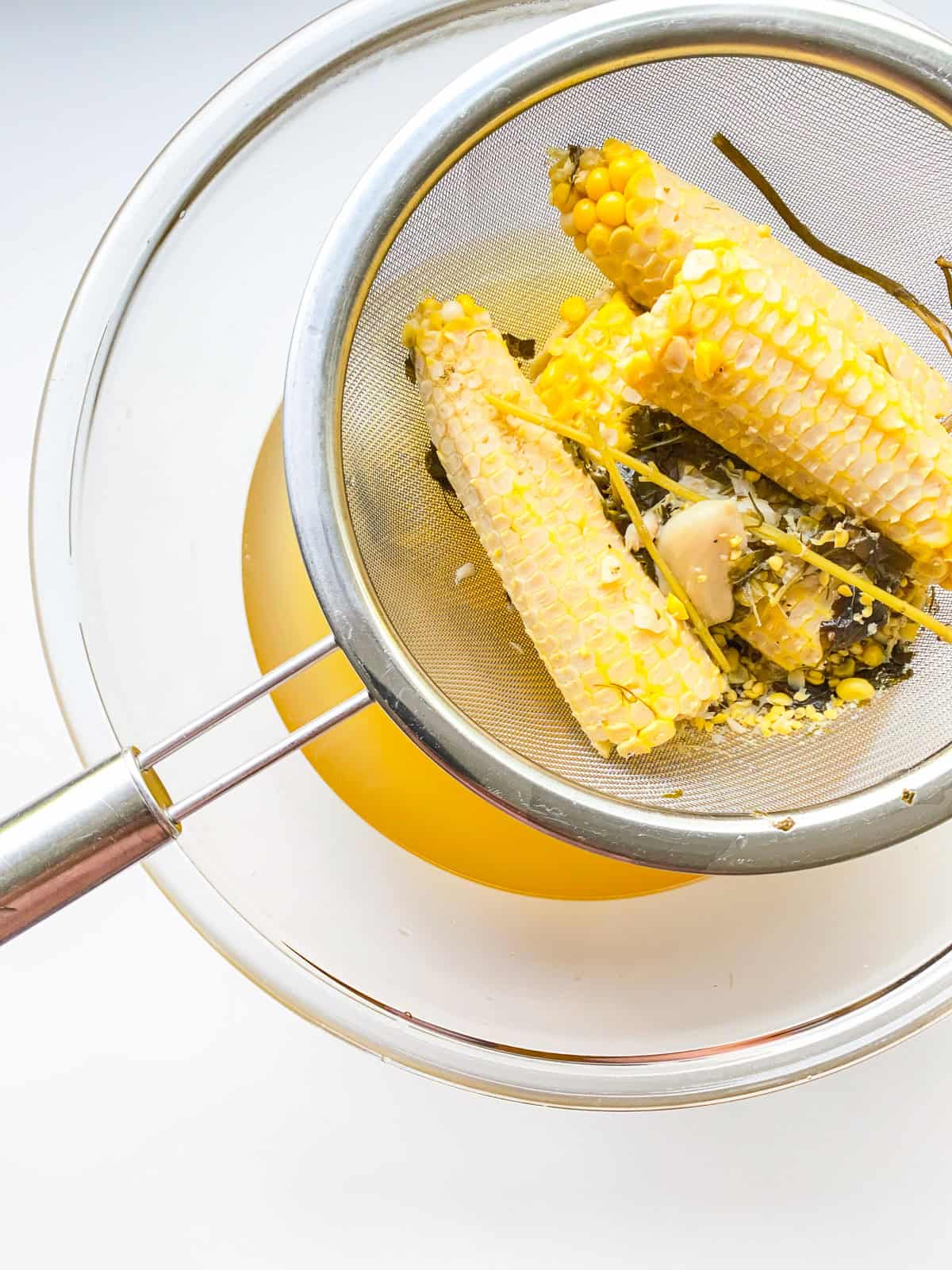 An image of corn broth being strained over a glass bowl.