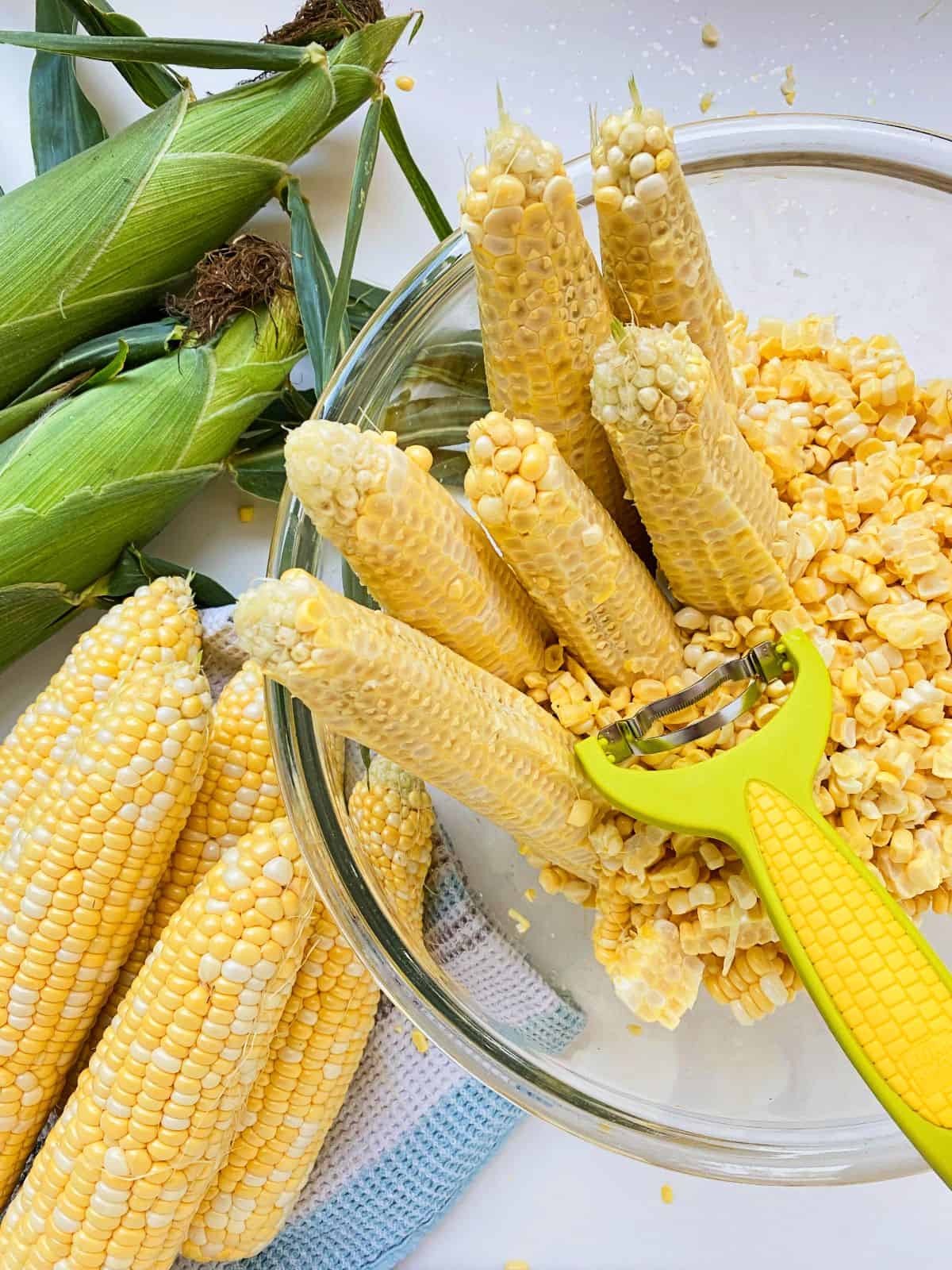 An image of fresh corn, corn that has been shucked, and a bowl containing striped cobs and their corn kernels alongside a corn zipper gadget.