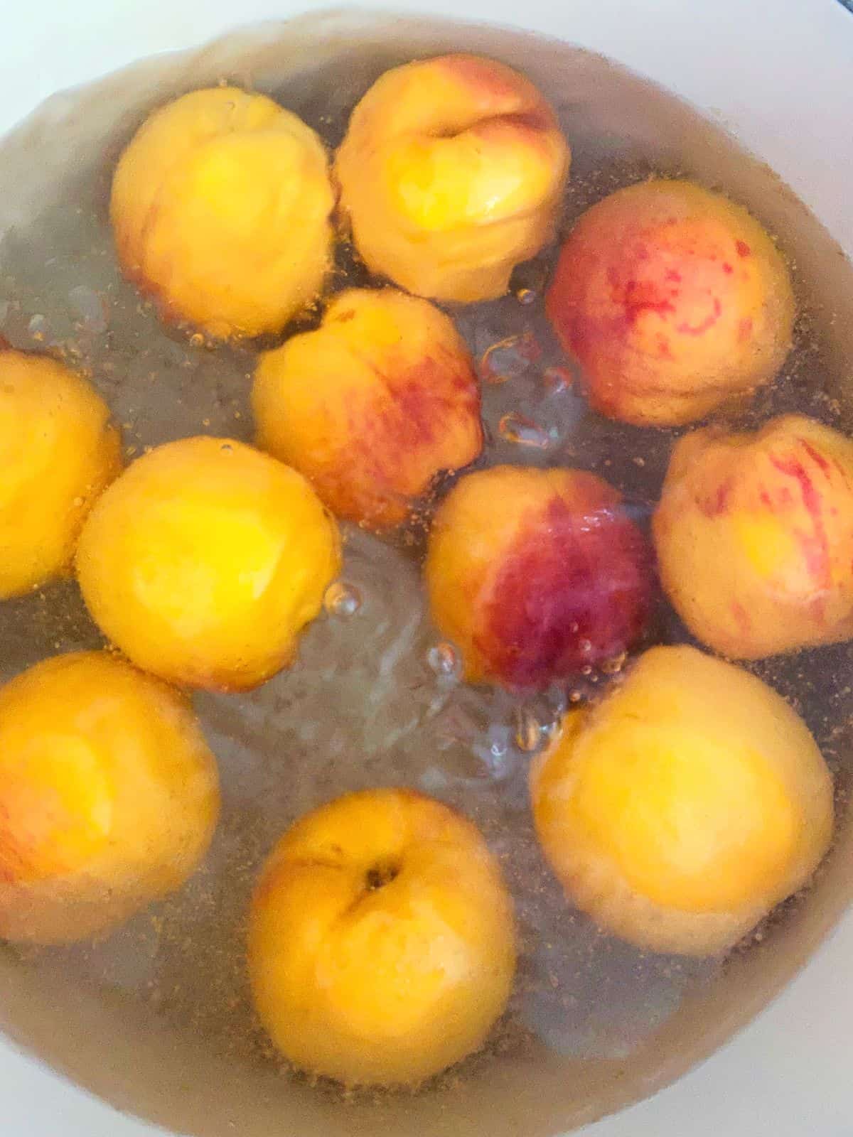 An image of peaches being blanched in a pot of boiling water.
