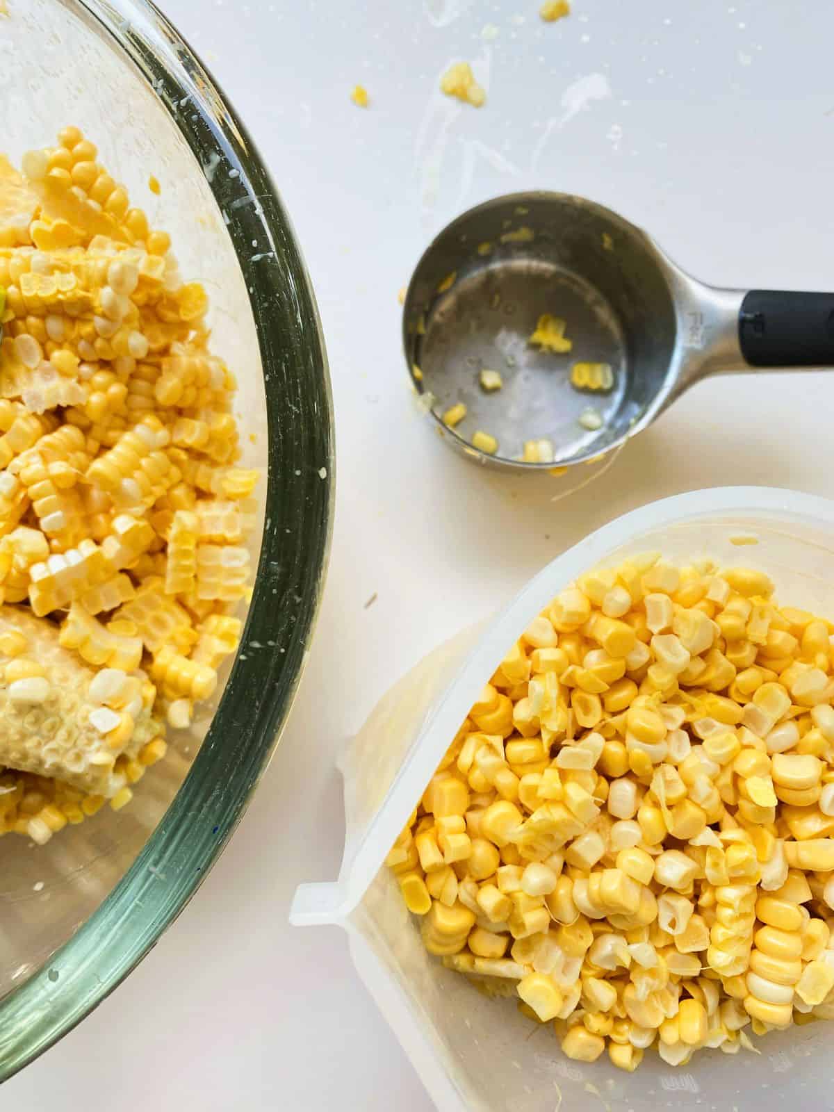An image of a bowl of corn kernels, a measuring cup, and a partially filled silicone pouch filled with corn kernels ready for the freezer.