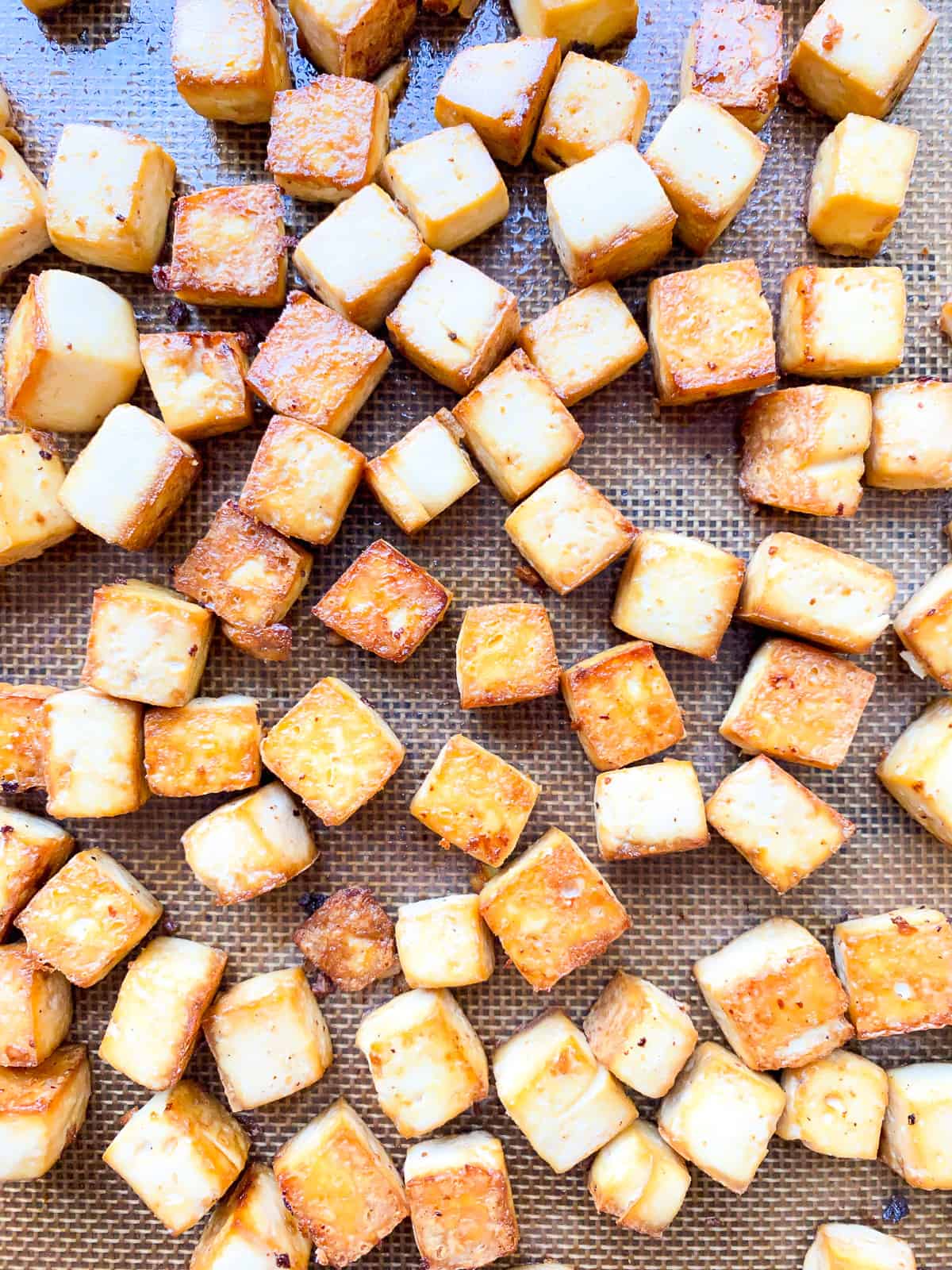 A close up image of baked tofu cubes on a baking tray lined with a silicone mat.