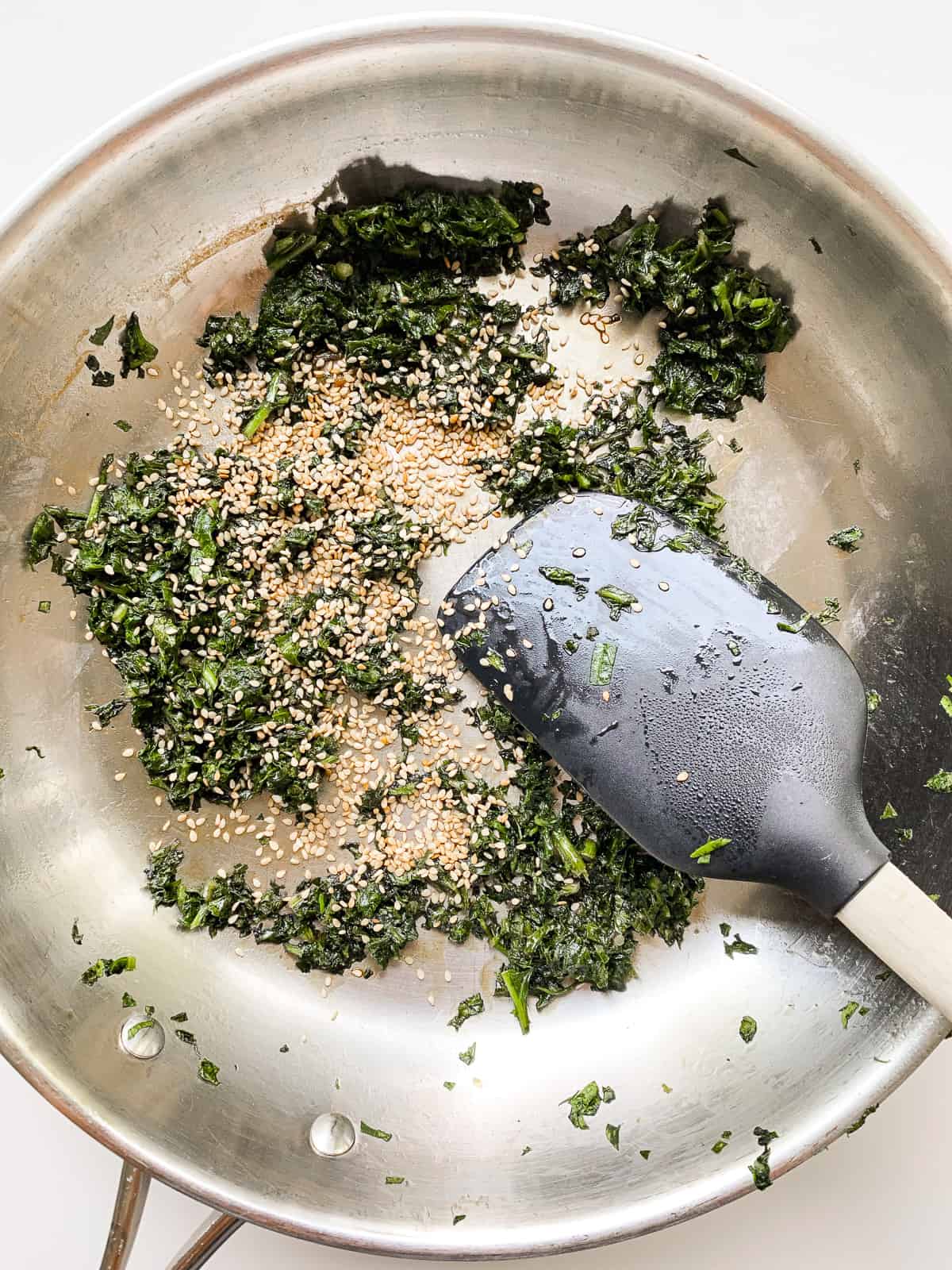 An image of greens and sesame seeds in a pan being cooked.