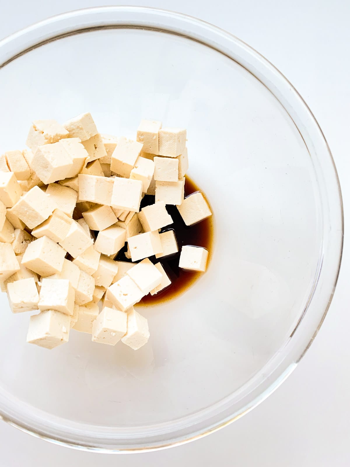 An image of tofu cubes in a glass bowl with a marinade.