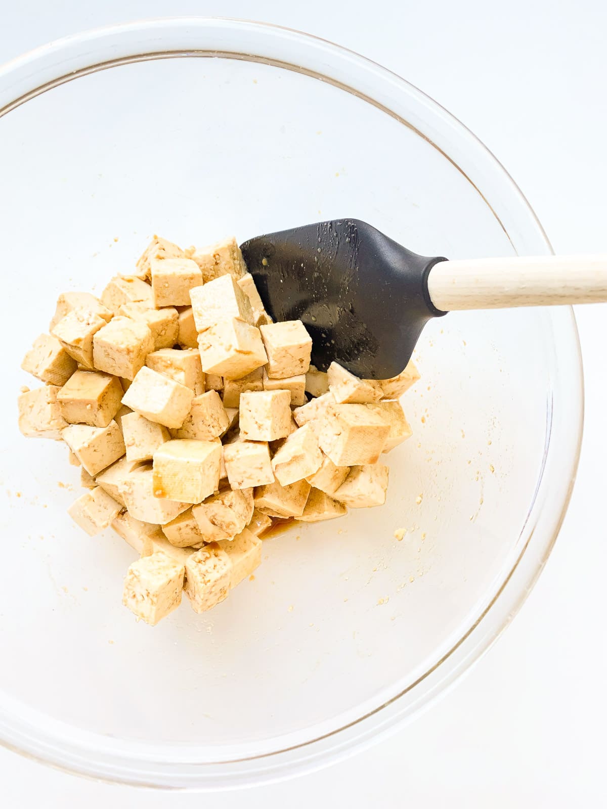 An image of tofu cubes in a glass bowl after being tossed in a marinade.