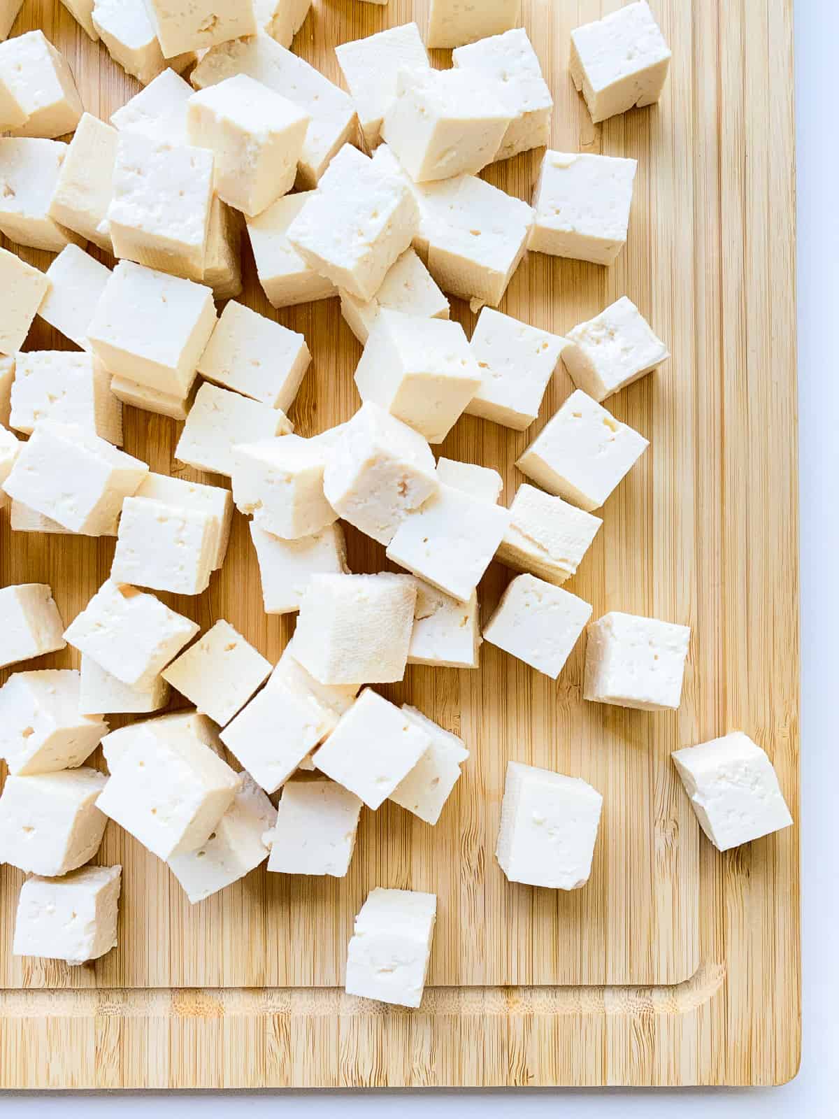 An image of tofu cubes on a bamboo cutting board.