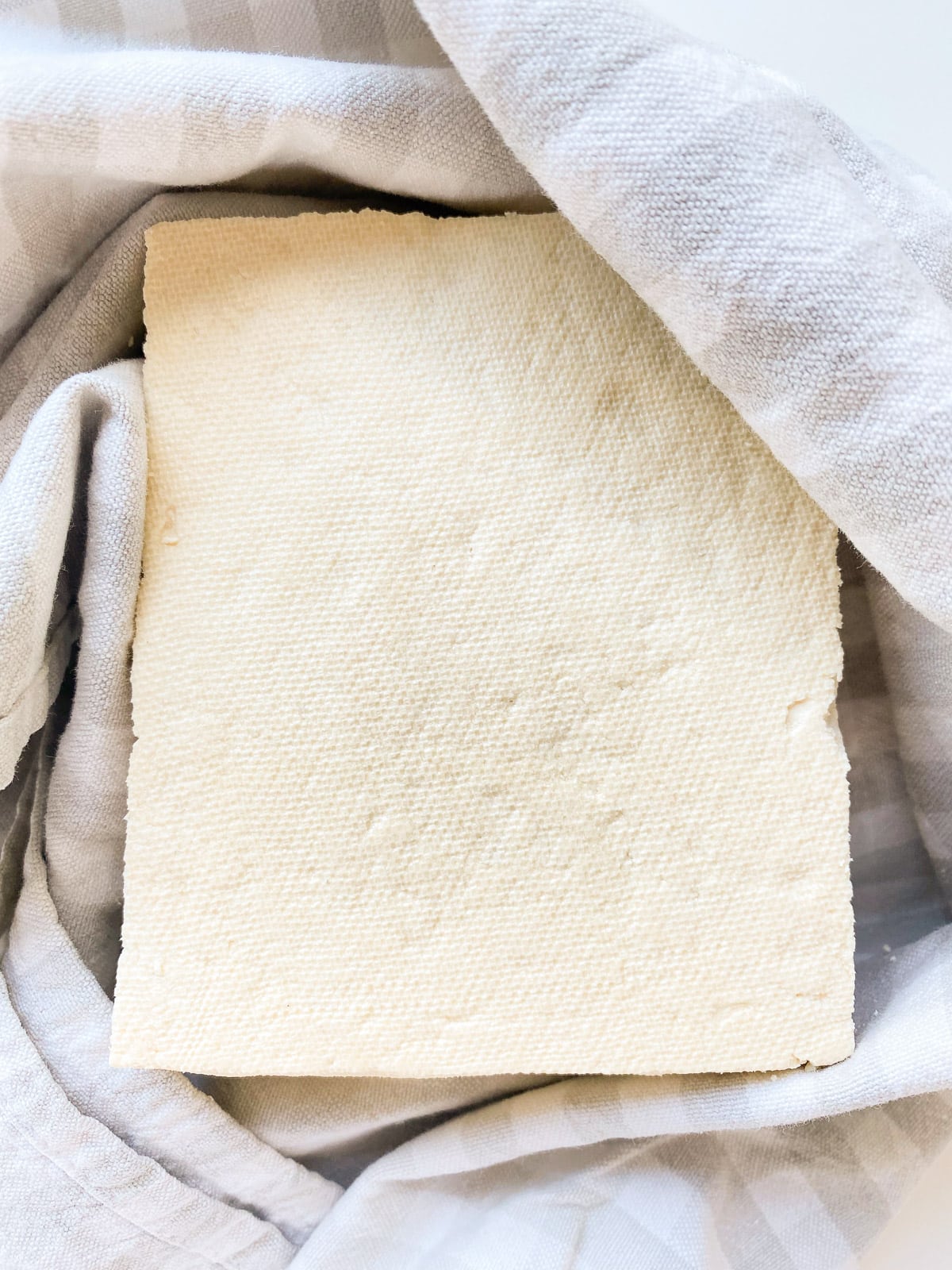 An image of a block of tofu being dried in a clean tea towel.