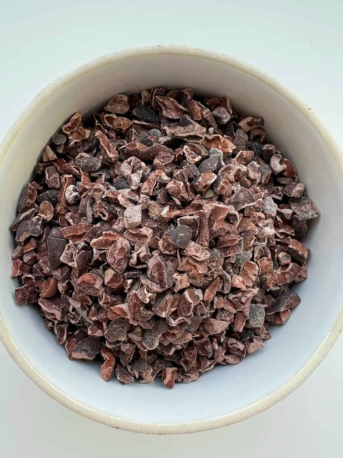 A white ceramic bowl contains cacao nibs.