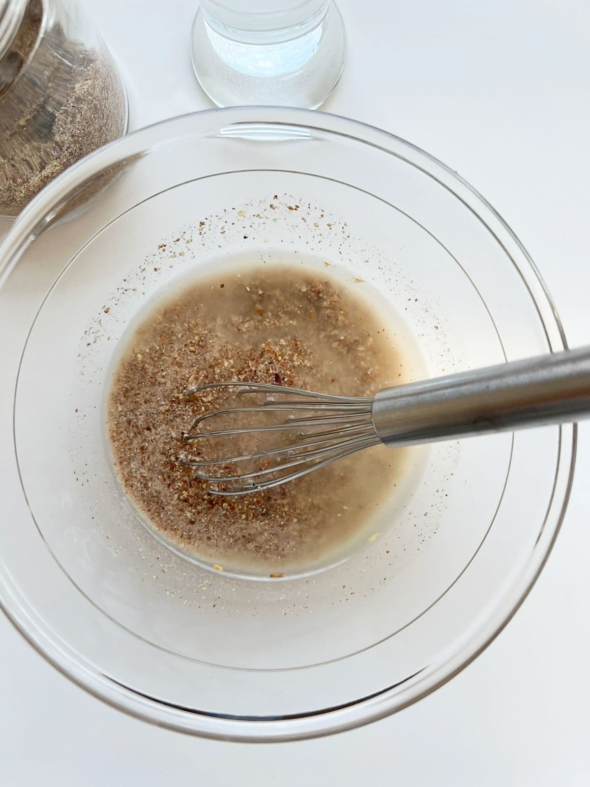 An image of ground flaxseed and water mixed together in a glass bowl with a silver whisk.