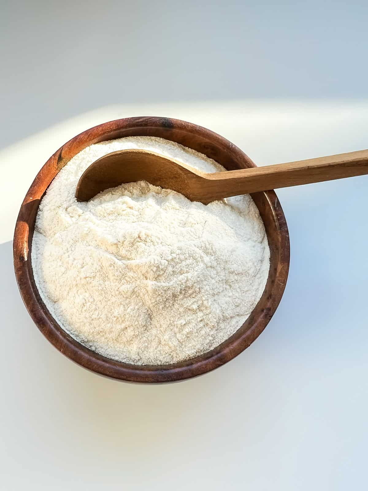 A wooden bowl heaped with cream coloured malt powder.