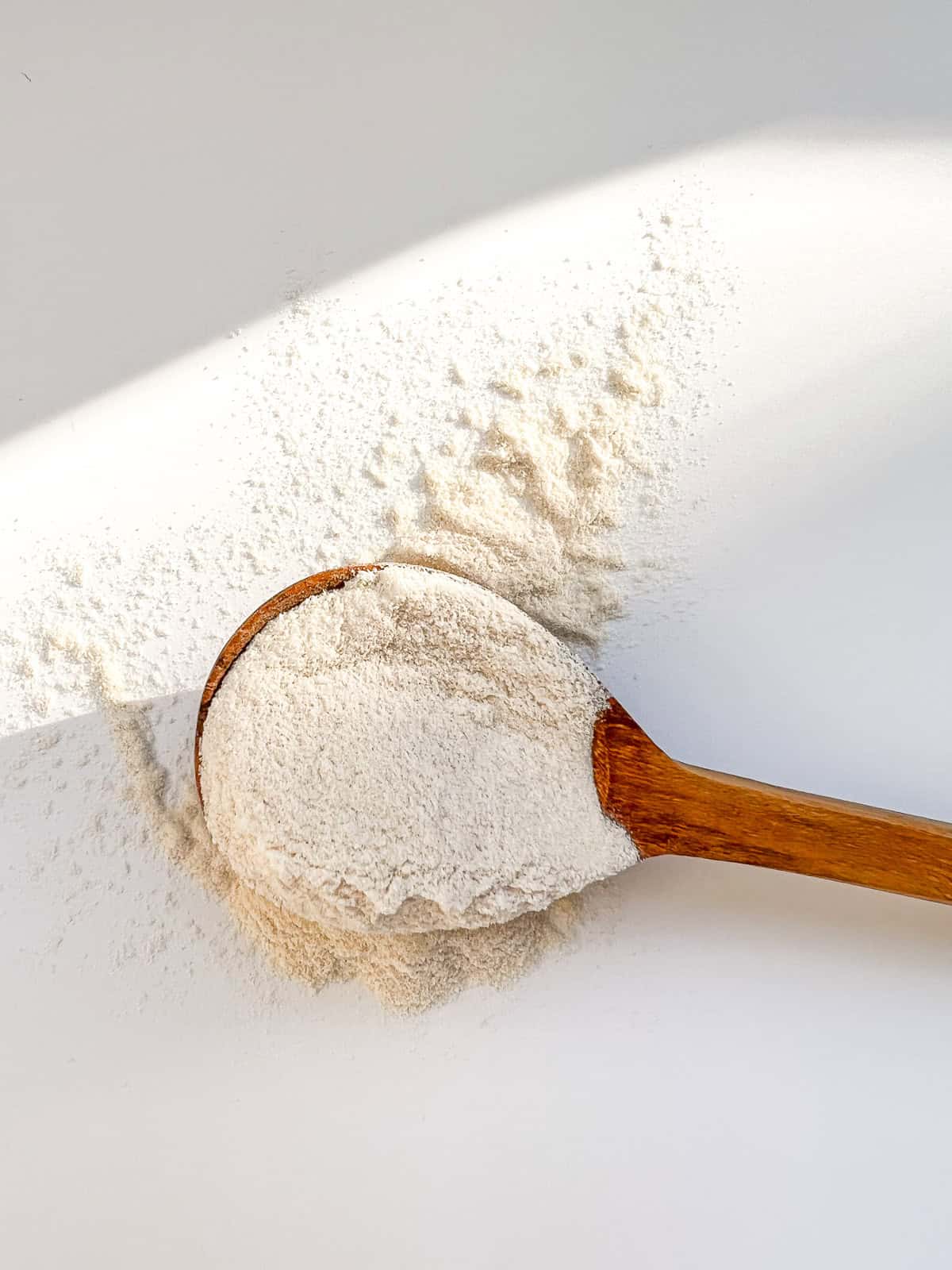 A wooden spoon heaped with cream coloured malt powder.