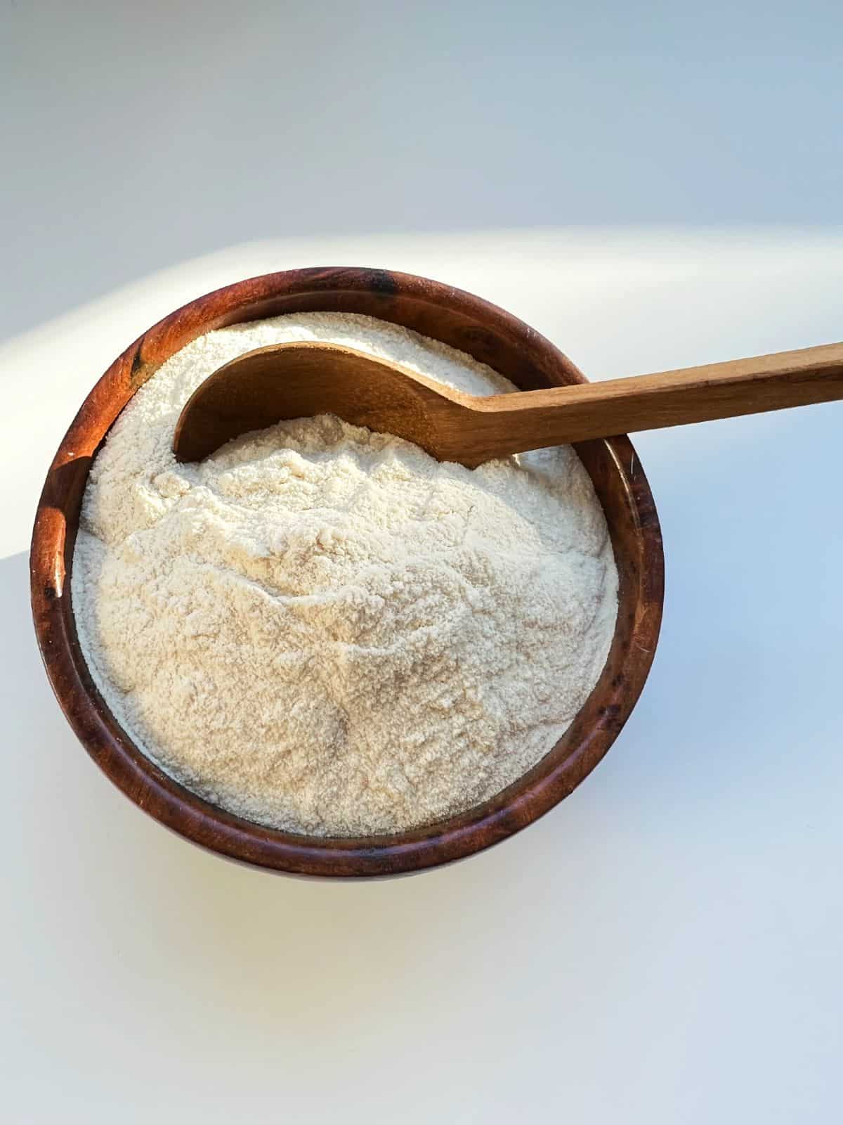 A wooden bowl heaped with cream coloured malt powder.