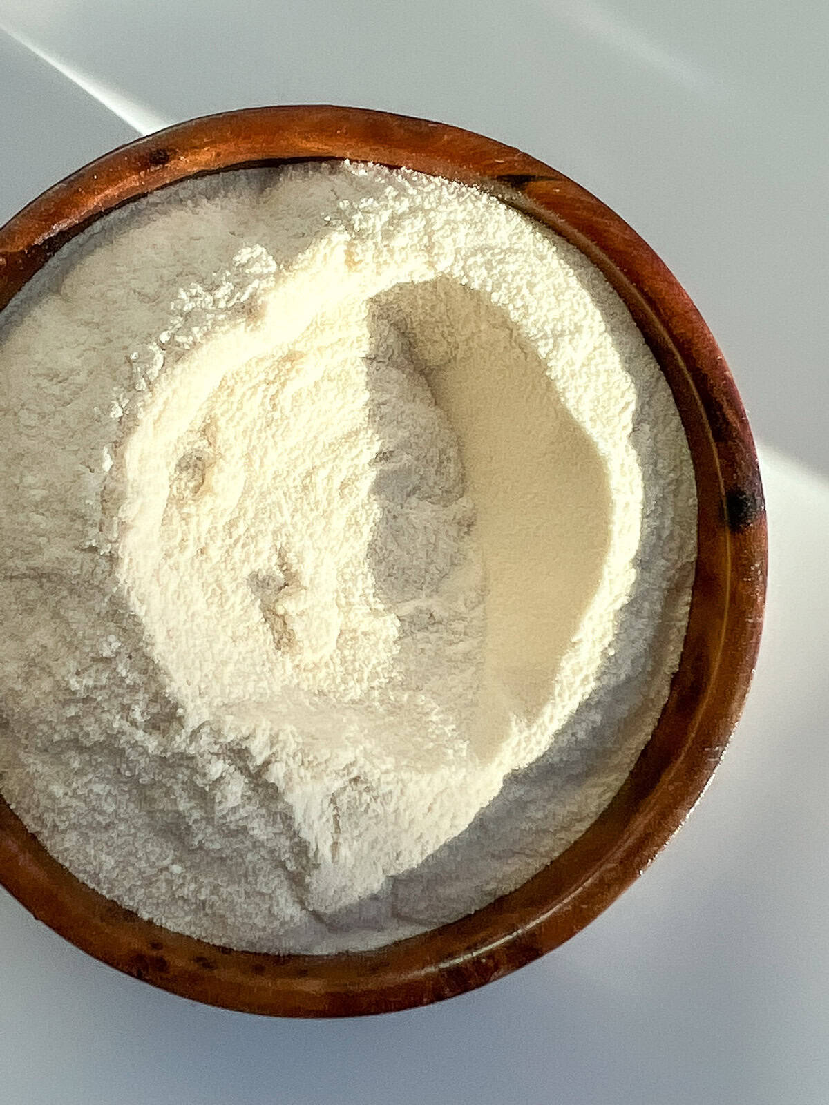 A wooden bowl heaped with cream coloured malt powder.