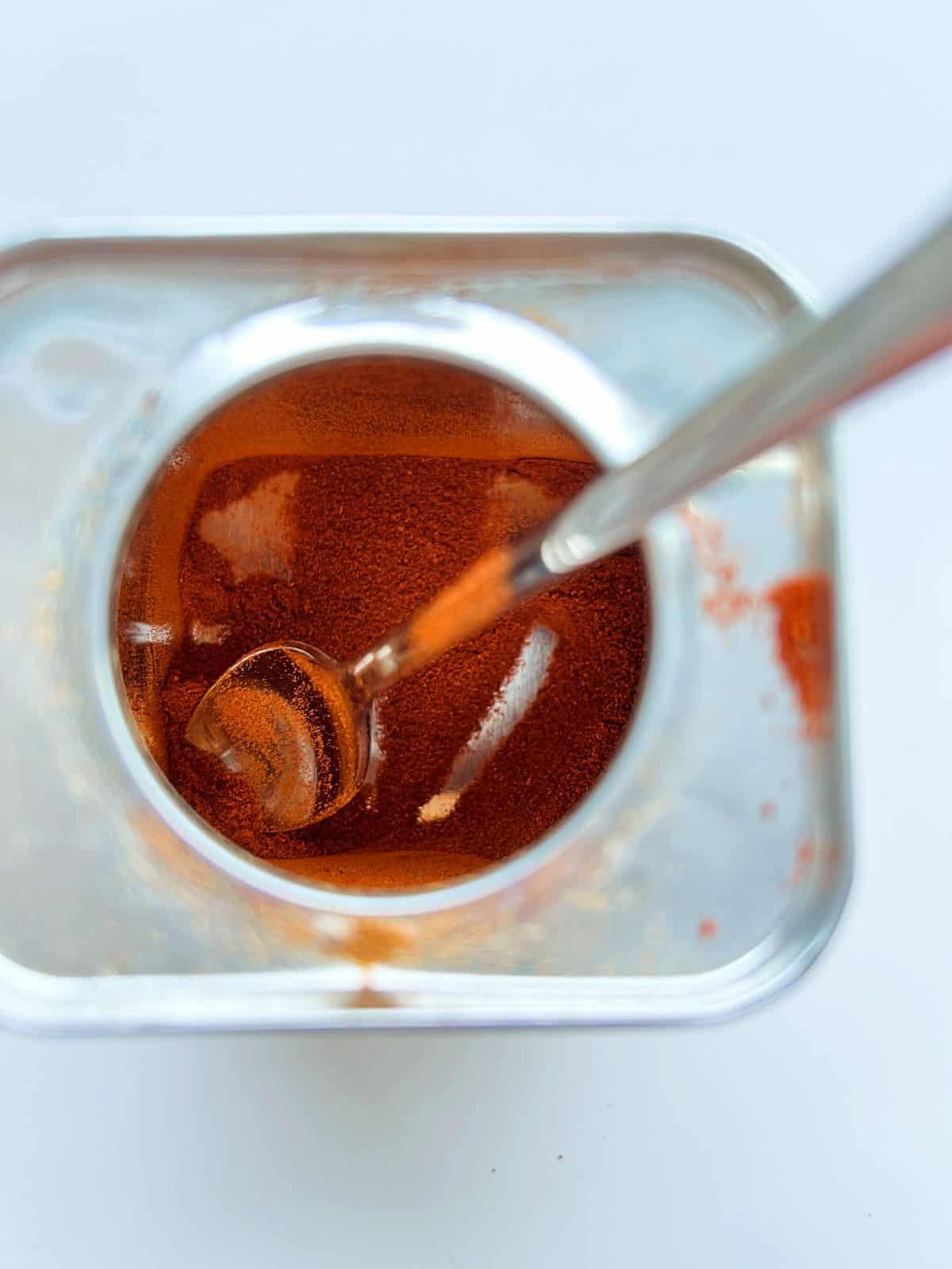 An image of spanish smoked paprika in a small tin with a spoon sticking out of the top opening of the tin.