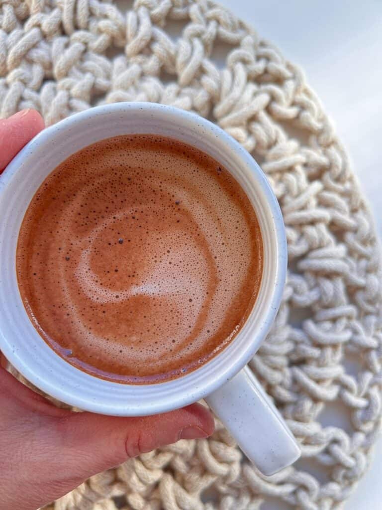 An image of a hand holding a mug of Hot Malted Cacao.
