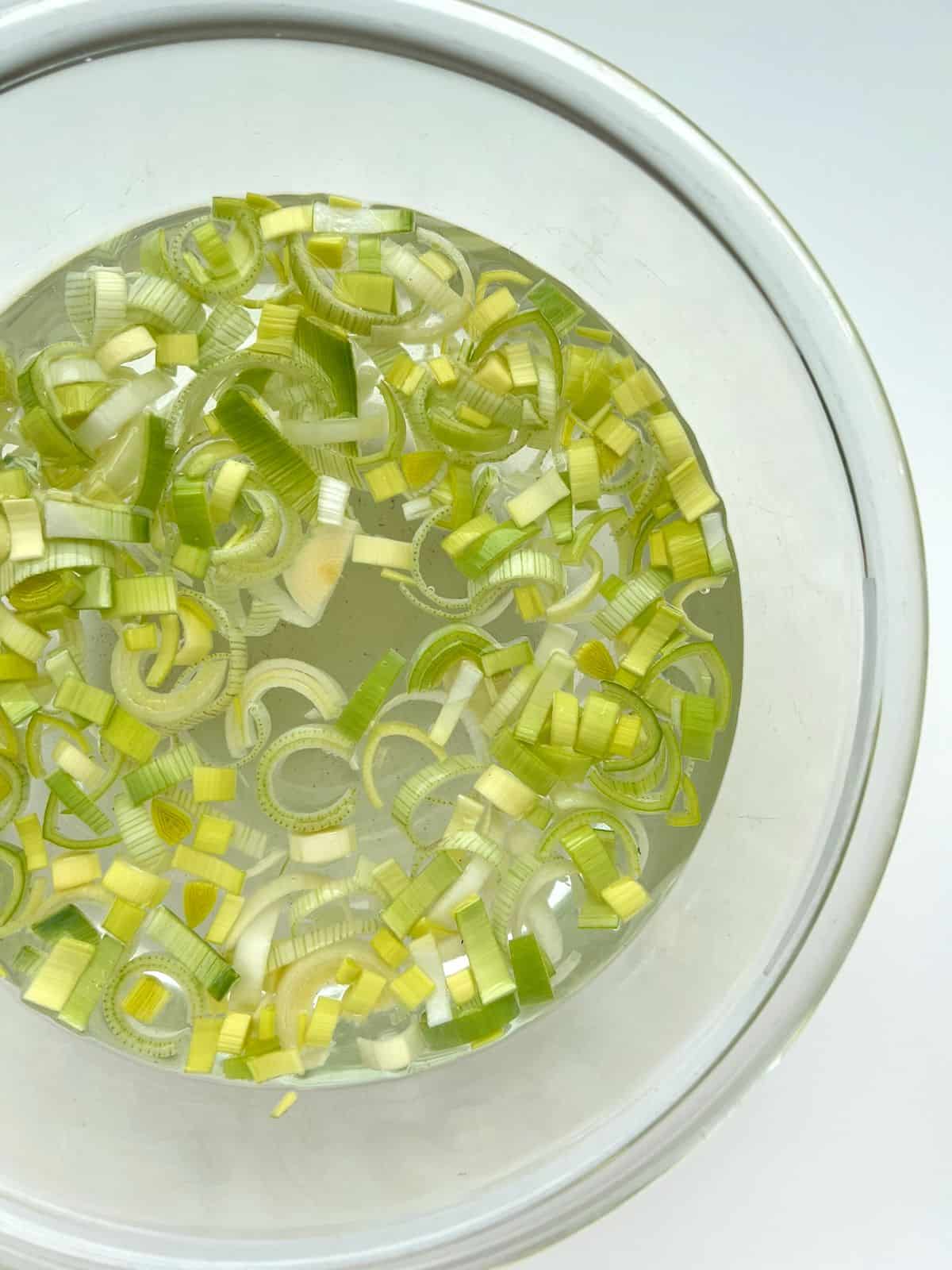 Cut leeks soaking in water in a glass bowl.