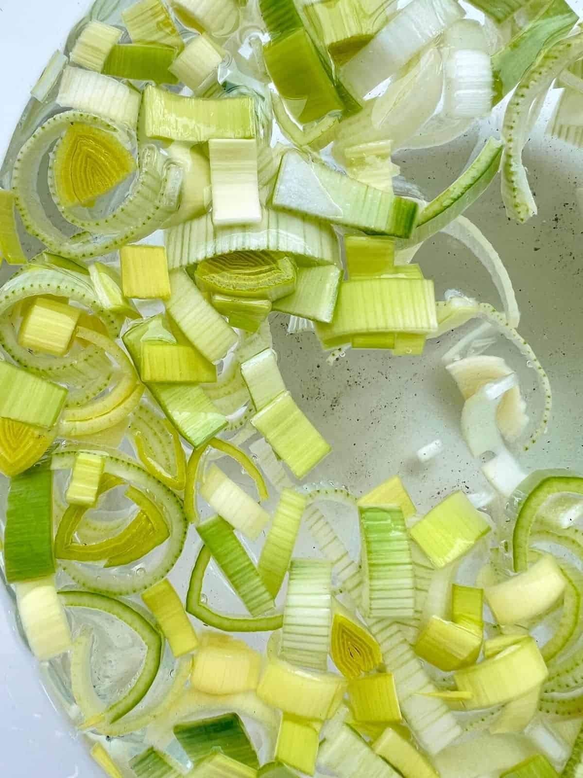 A close up of cut leeks soaking in water in a glass bowl.