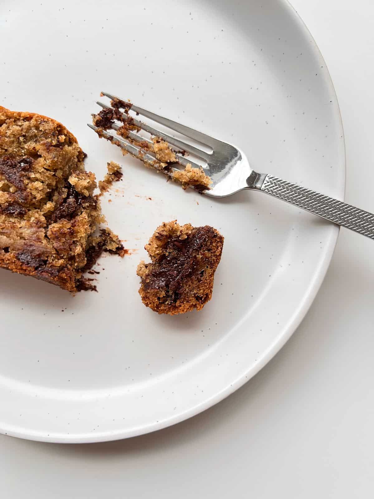An image of a partially eaten slice of Super Chocolatey Banana bread on a cream coloured plate with a silver fork nearby.