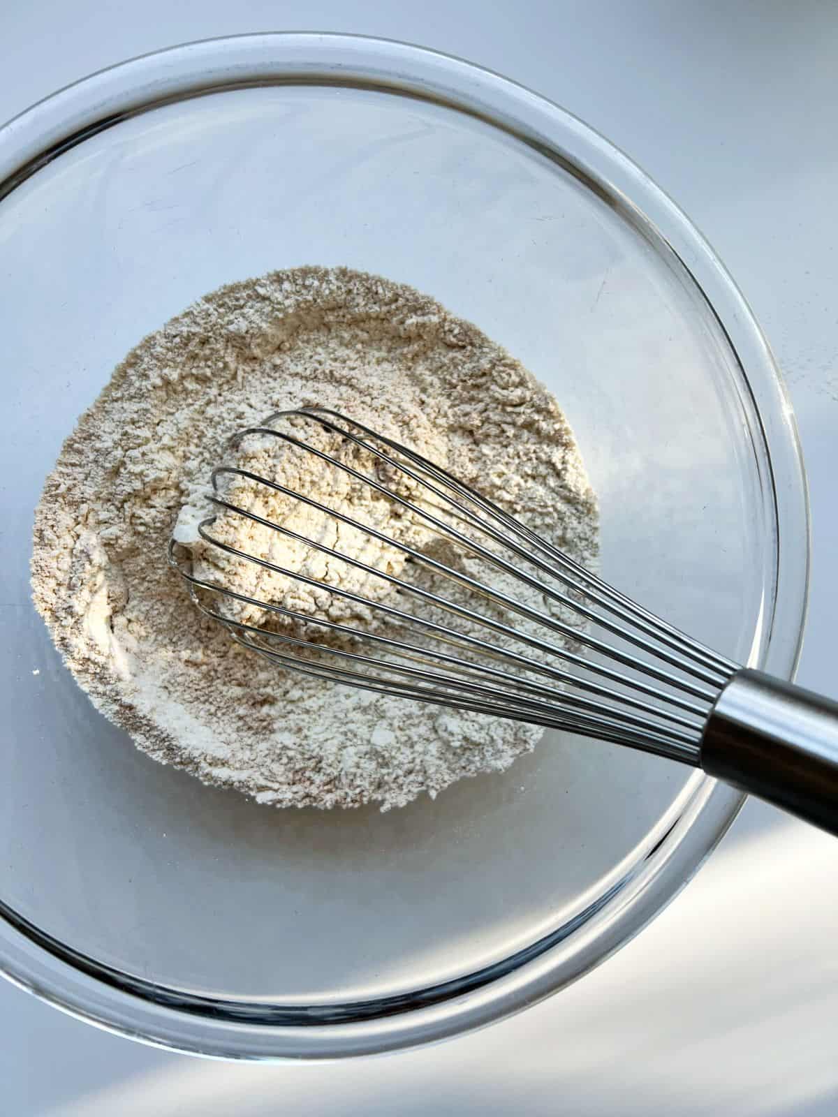 An image of the dry ingredients need for the recipe, in a glass bowl with a wire whisk.