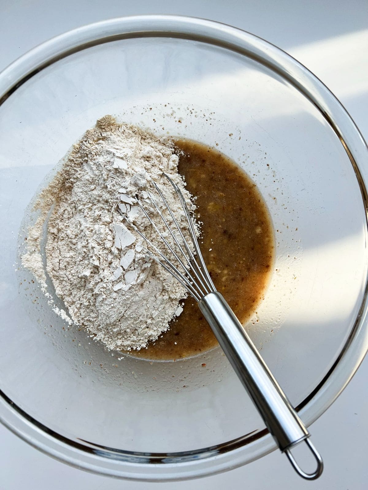 An image of the wet ingredients need for the recipe, whisked in a glass bowl with the dry ingredients added on top.