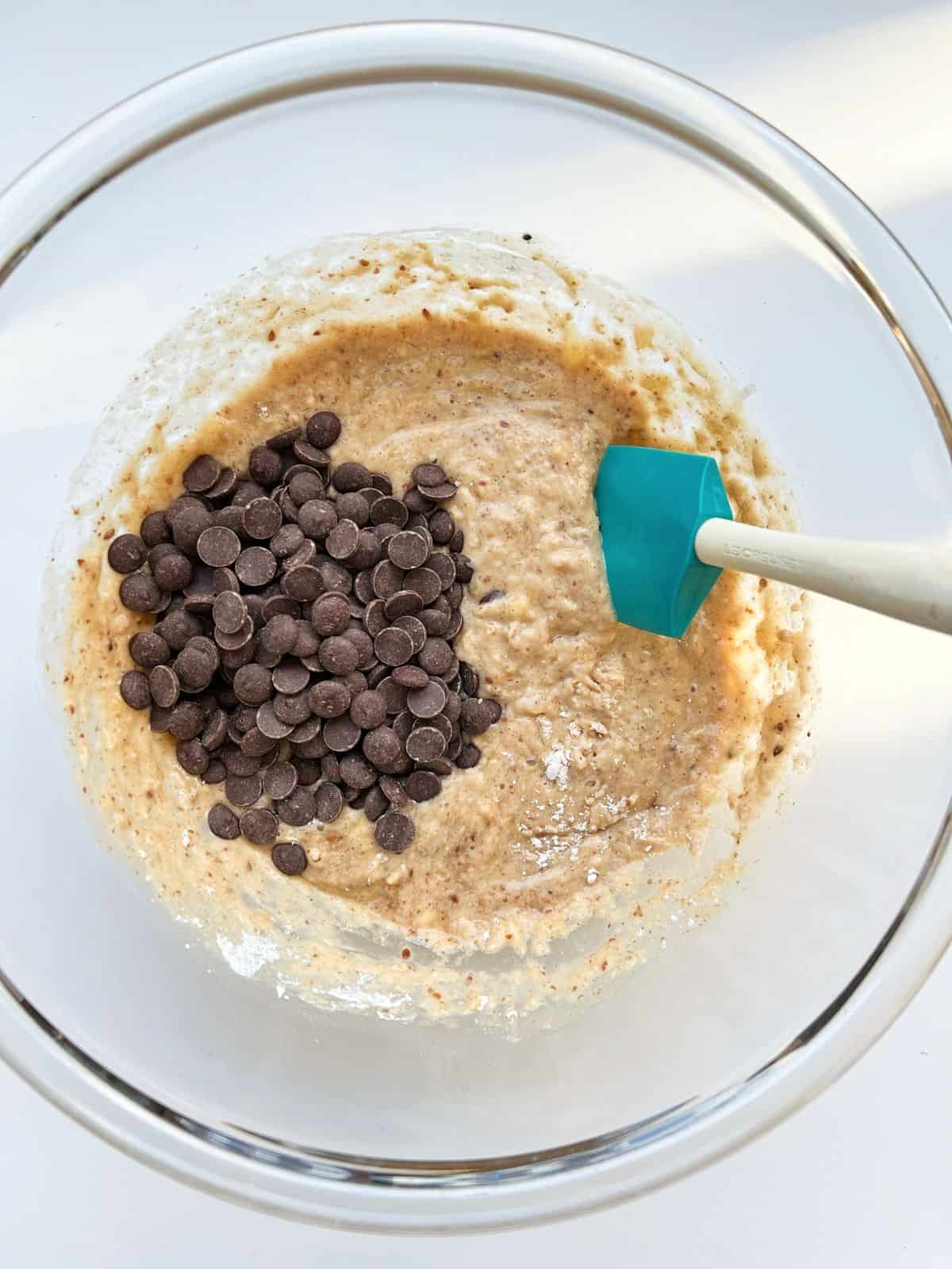 An image of the whisked mix for the banana bread in a glass bowl, with chocolate chips sitting on top.
