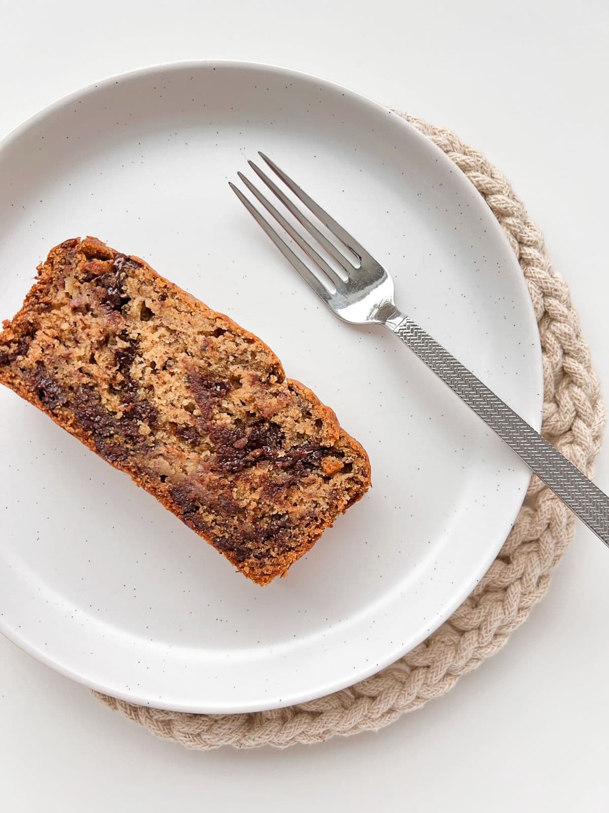 An image of slice of Super Chocolatey Banana Bread sitting on a cream coloured plate with a silver fork nearby.
