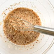 An image of ground flaxseed and water mixed together in a glass bowl with a silver whisk.