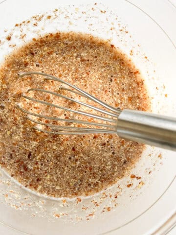 An image of ground flaxseed and water mixed together in a glass bowl with a silver whisk.