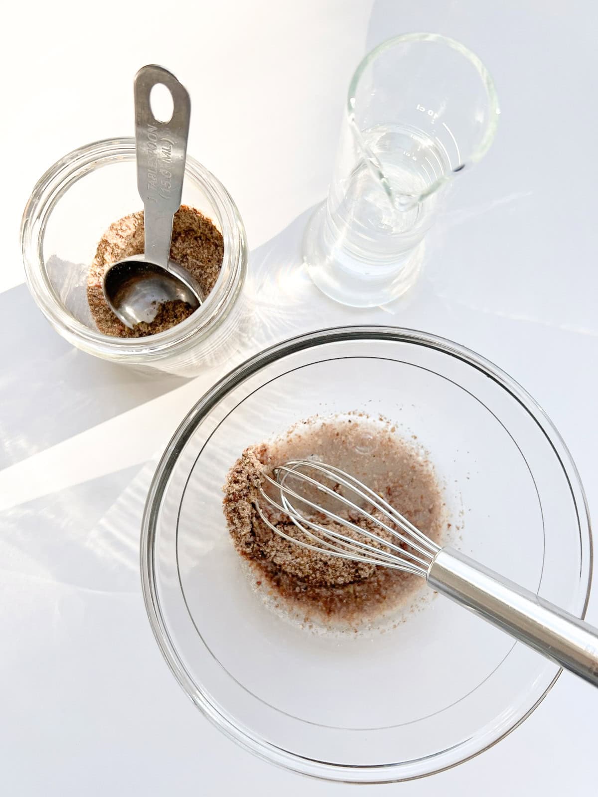 An image of ground flaxseed and water mixed together in a glass bowl with a silver whisk.