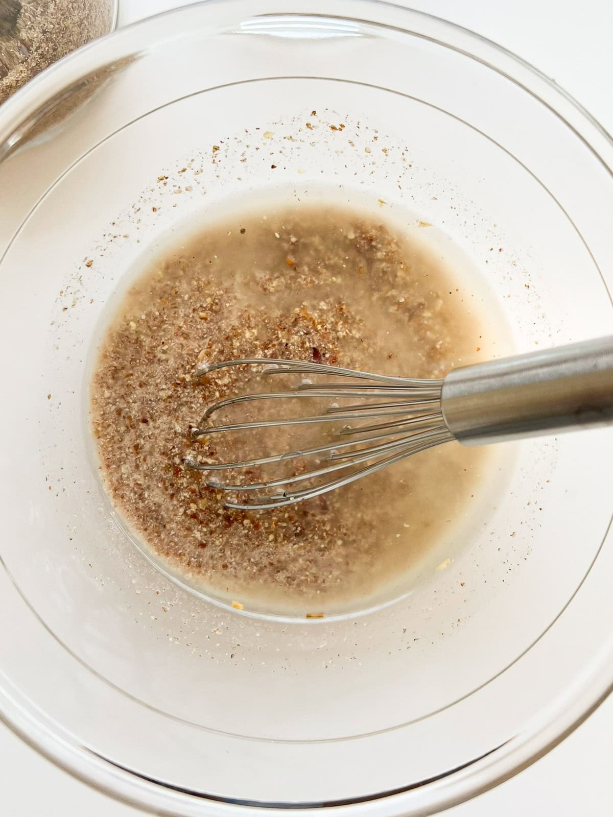 An image of ground flaxseed and water mixed together in a glass bowl with a silver whisk.