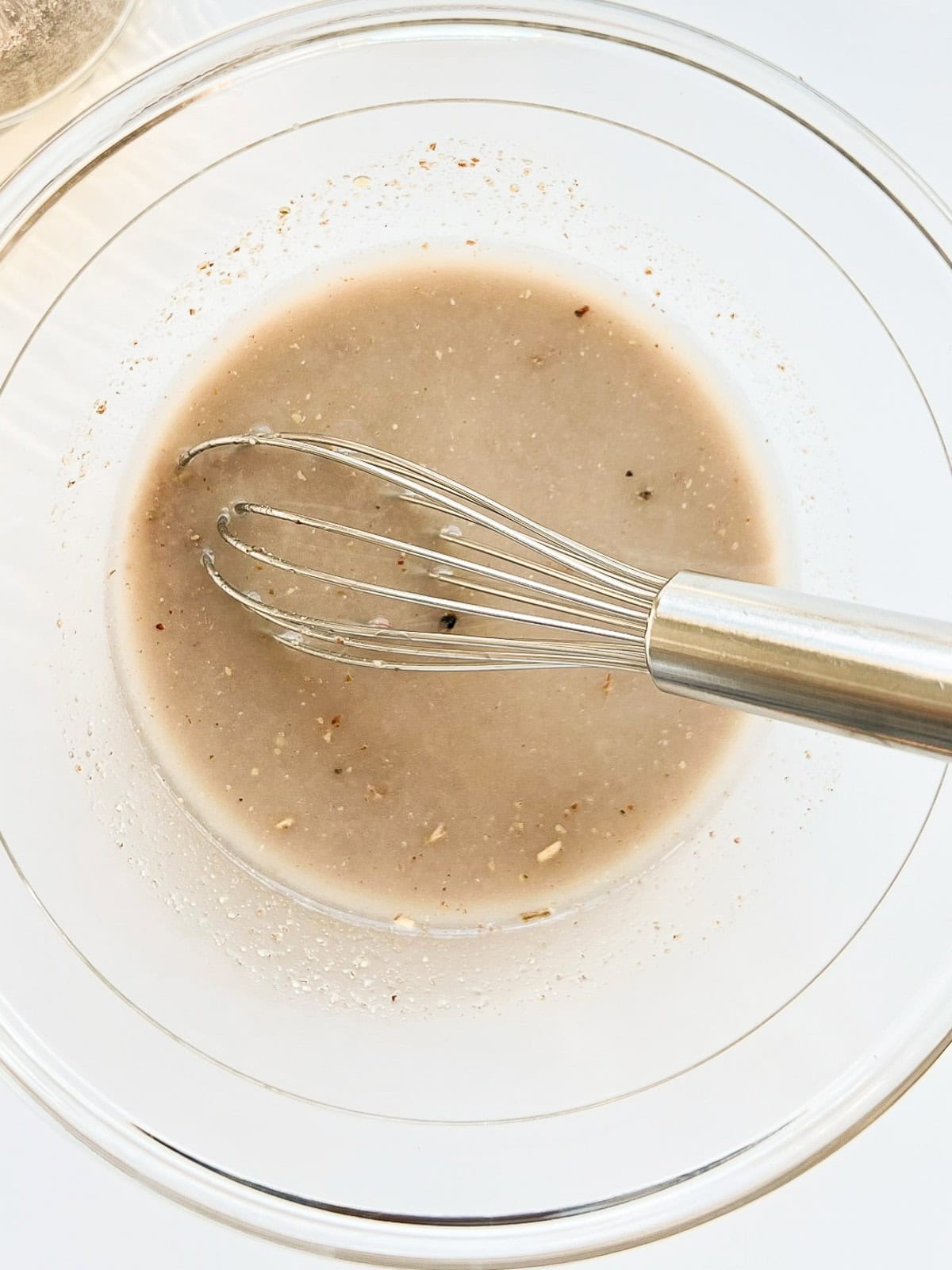 An image of ground flaxseed and water mixed together in a glass bowl with a silver whisk.