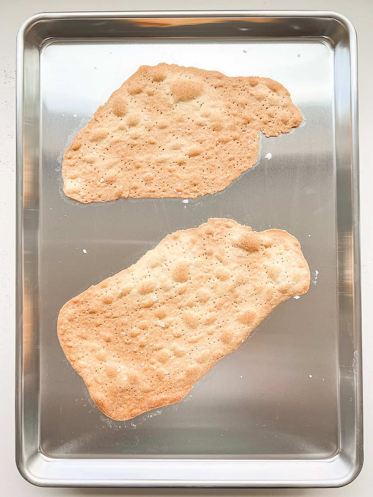 An image of two sheets of baked matzo on an aluminium baking sheet.