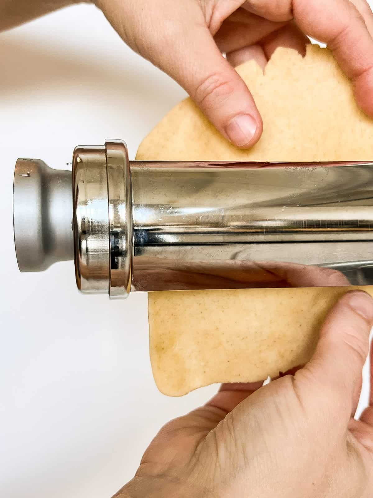 Dough being put through a pasta roller attachment on a stand mixer.