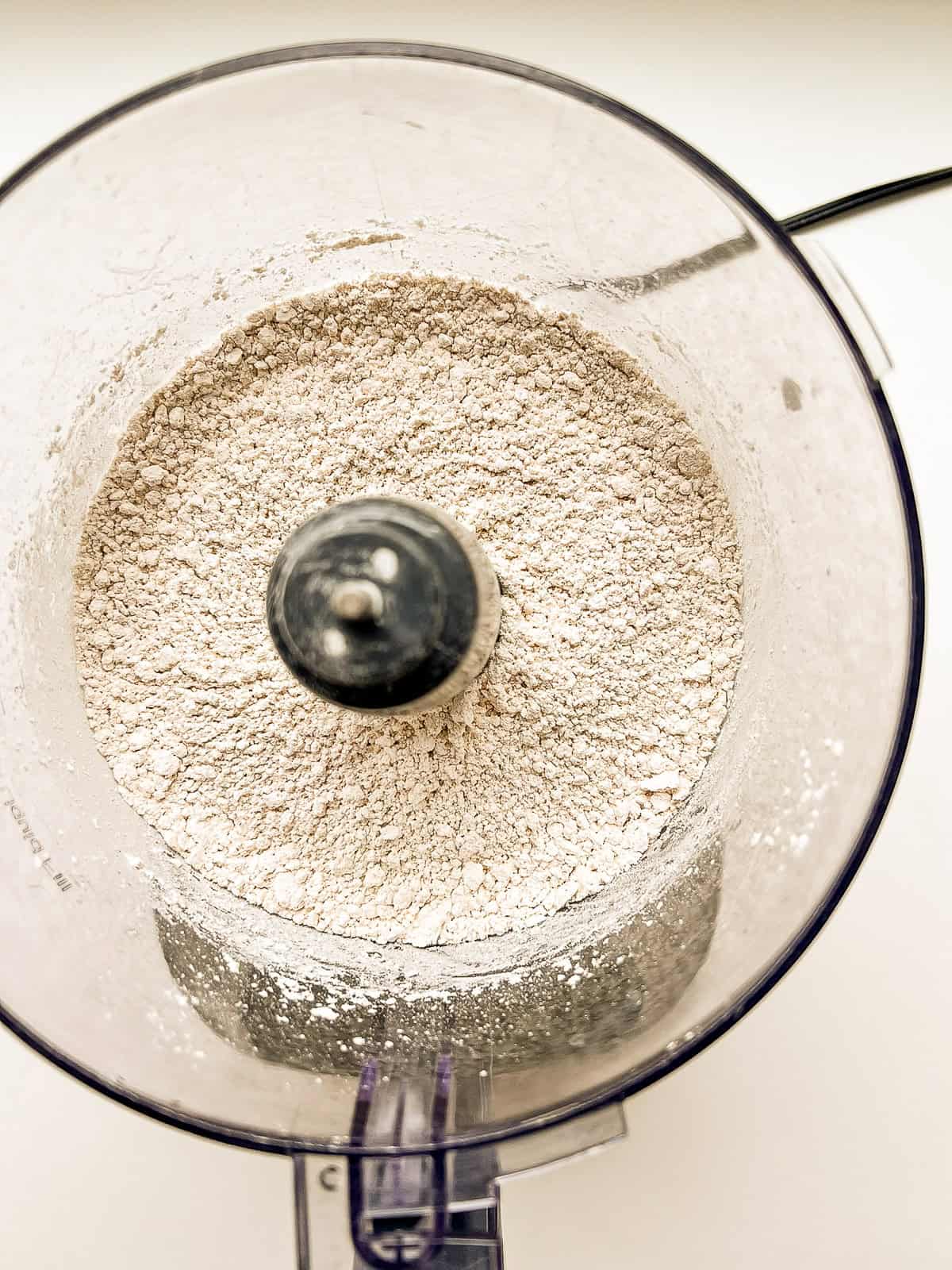 The bowl of a food processor with flour and salt inside.