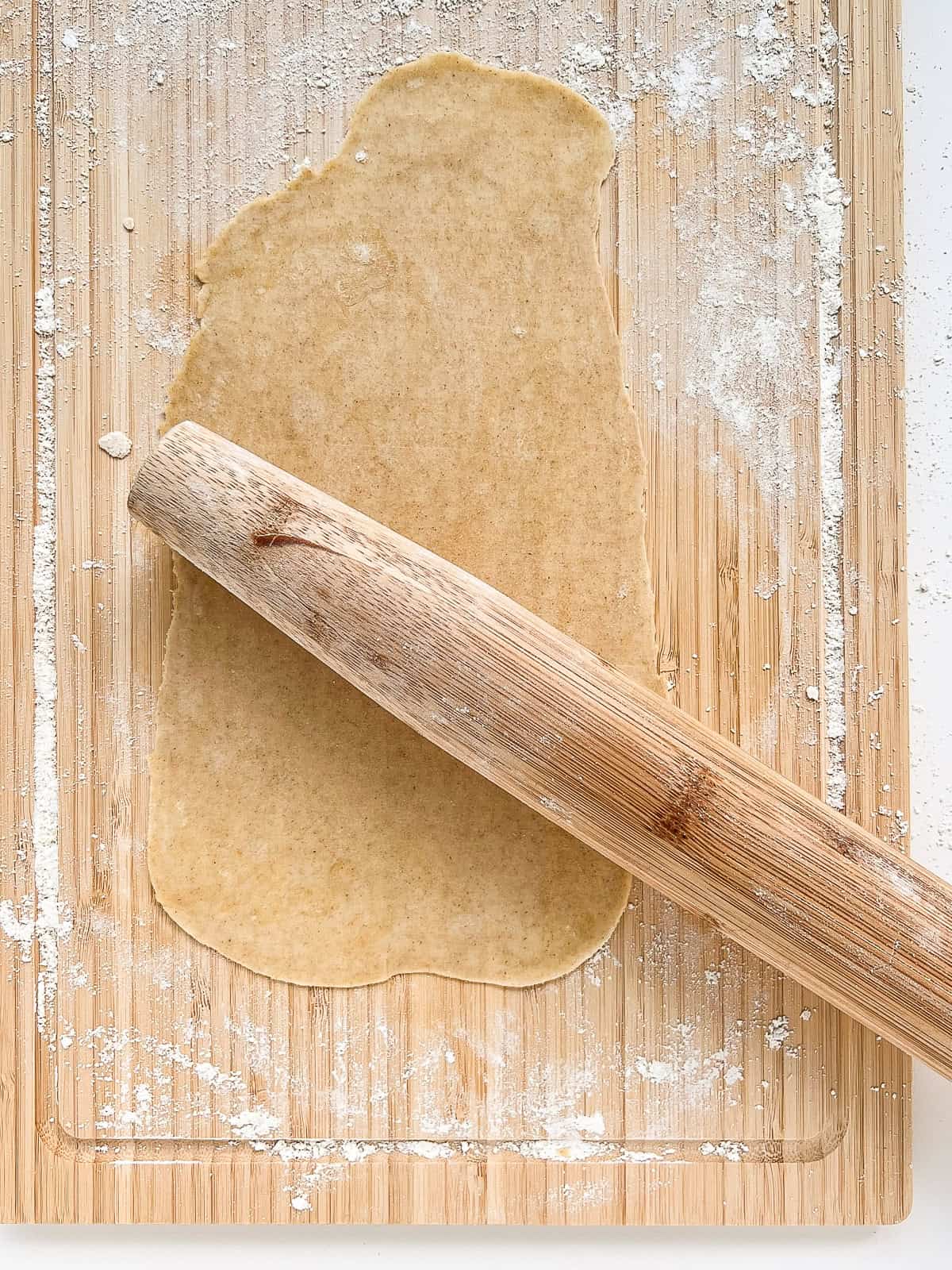 A sheet of matzo being rolled out on a bamboo cutting board.