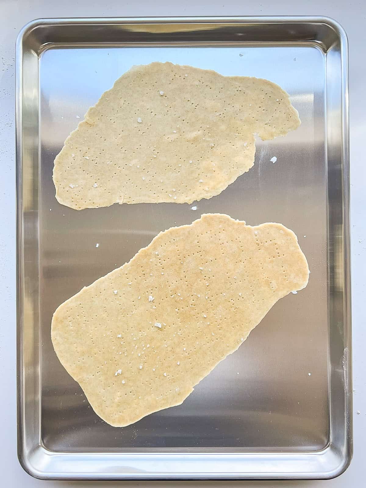 An image of two sheets of unbaked matzo on an aluminium baking sheet.