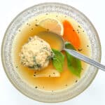 A serving of the matzo ball soup in a clear glass bowl.