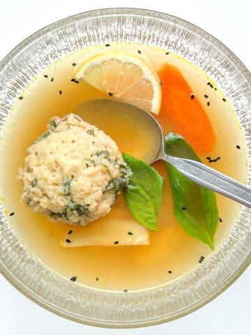 A serving of the matzo ball soup in a clear glass bowl.