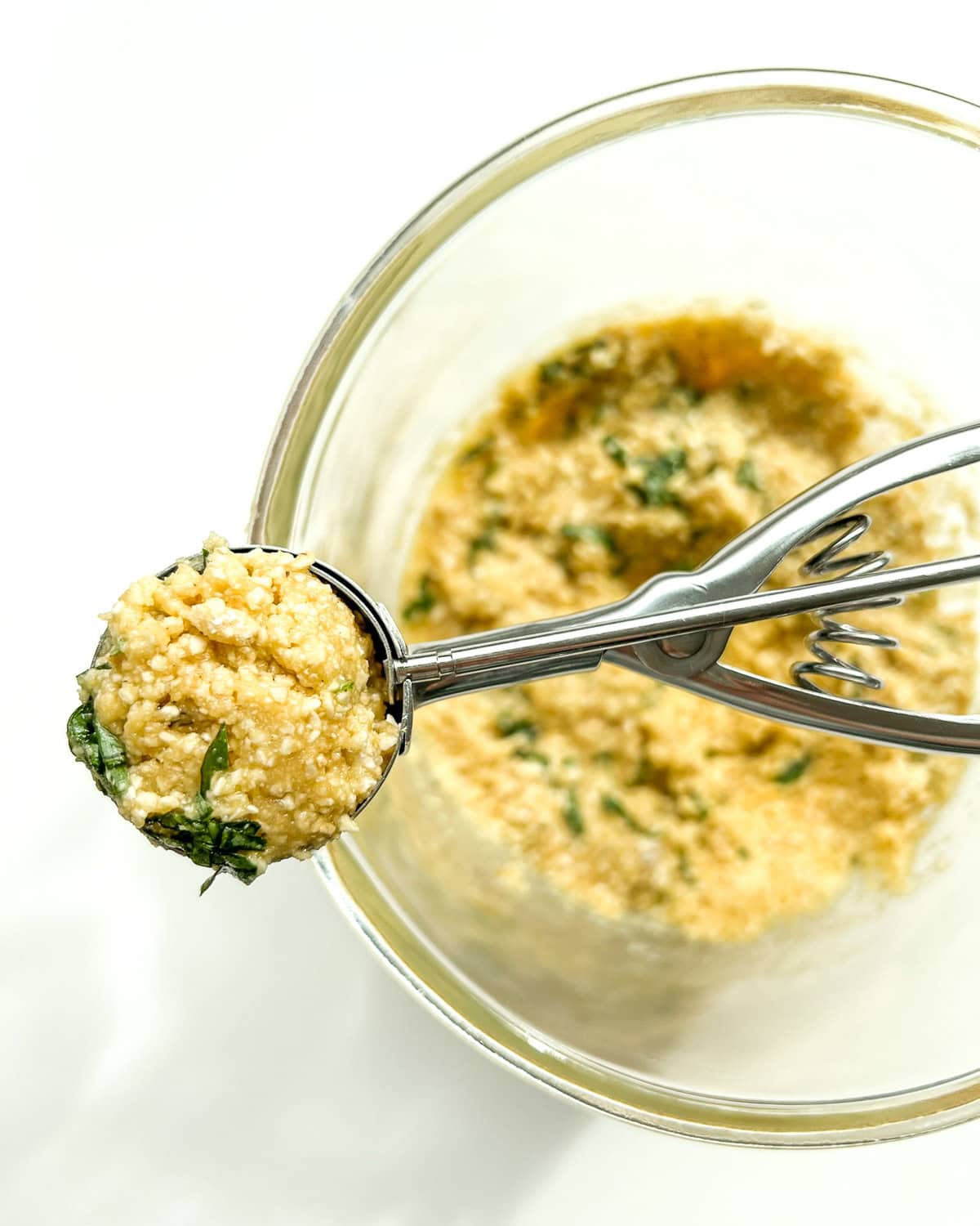 The finished matzo ball mixture being scooped up with a silver cookie scoop.