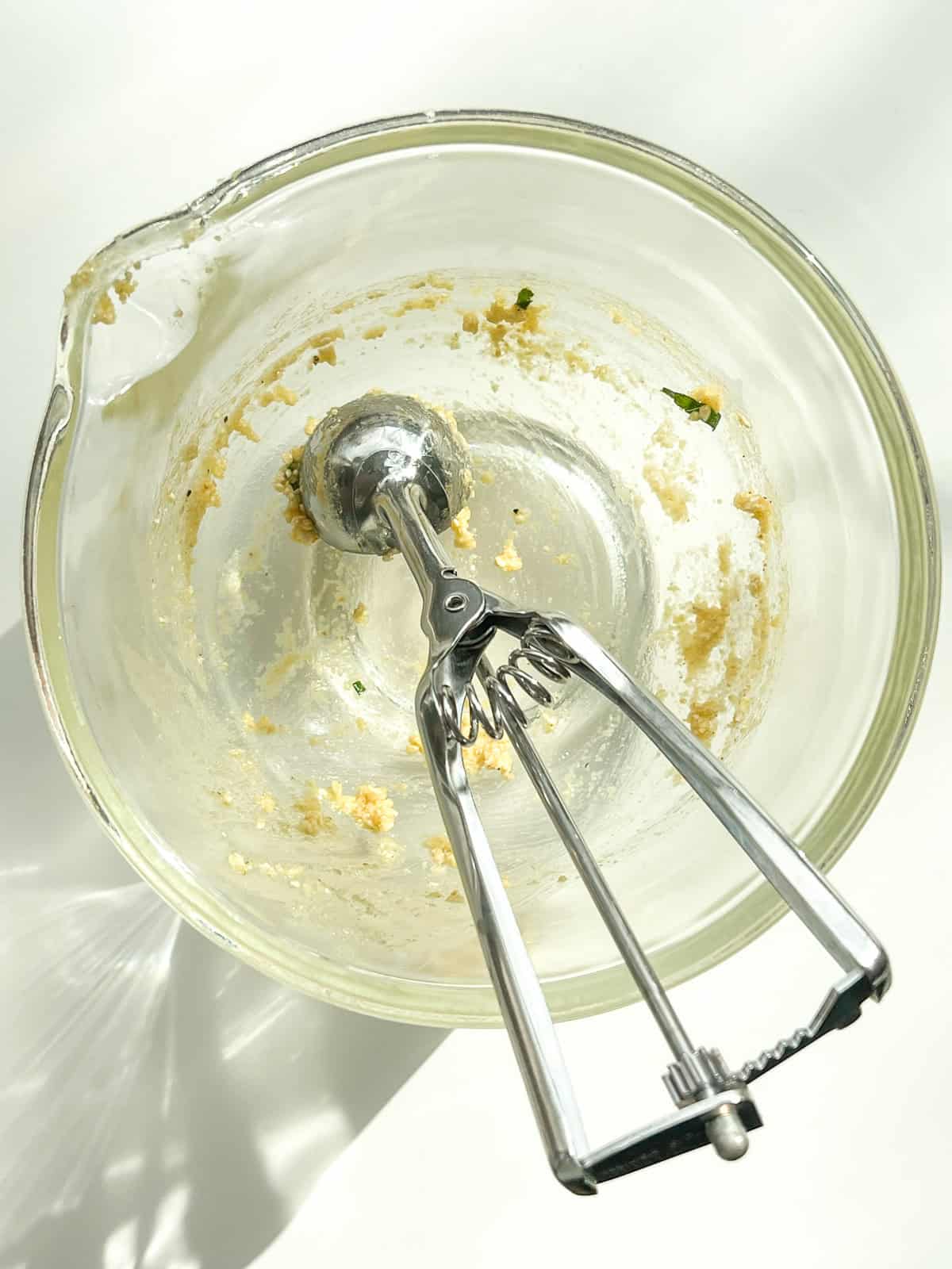 The bowl used for making the matzo ball mixture sitting empty with the scoop inside of it.