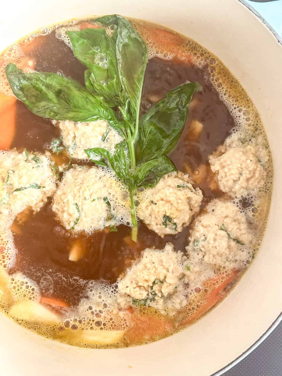 An image of the matzo balls cooking inside the broth, in a large enamel pot.