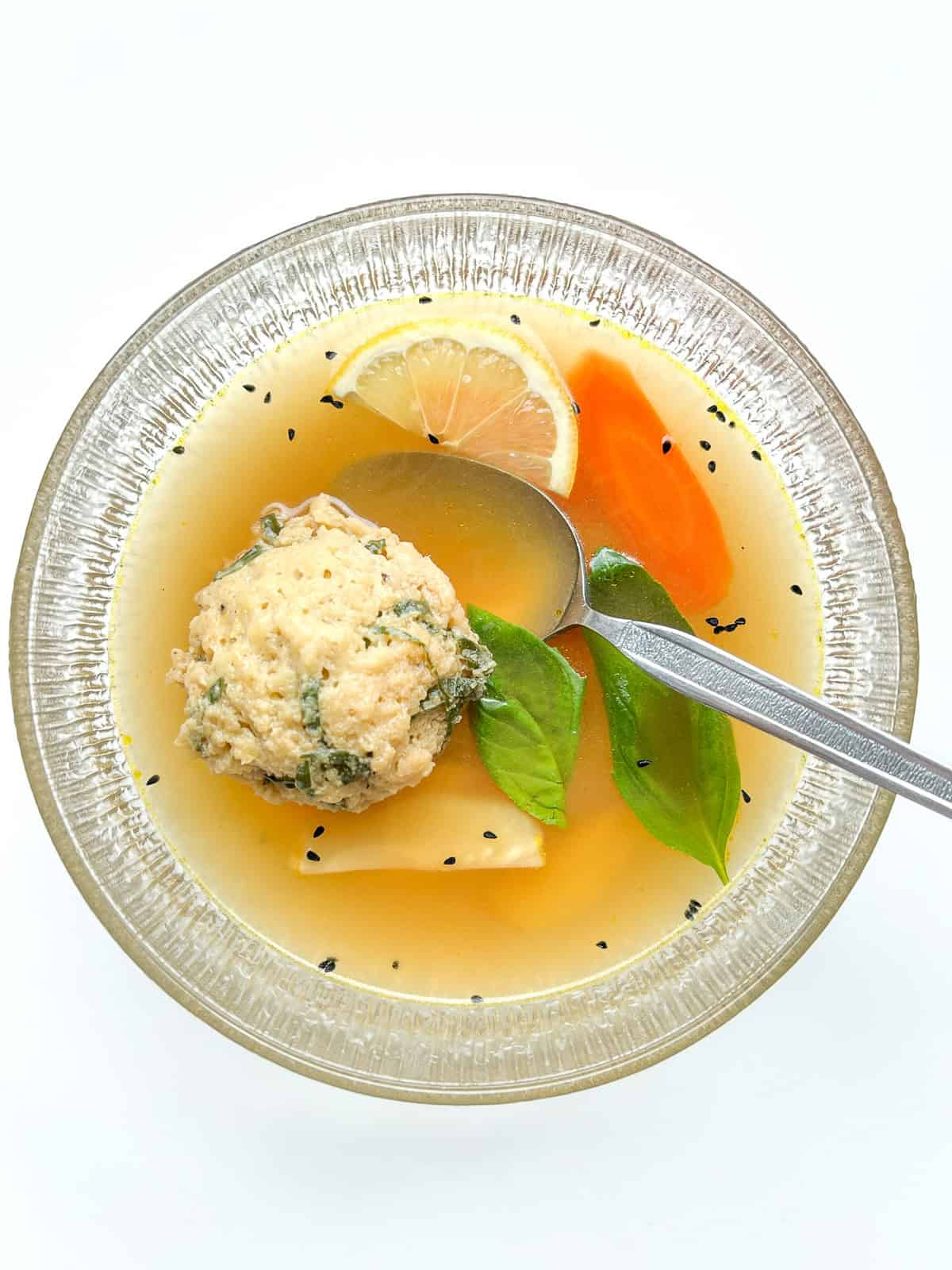 A serving of the matzo ball soup in a clear glass bowl.