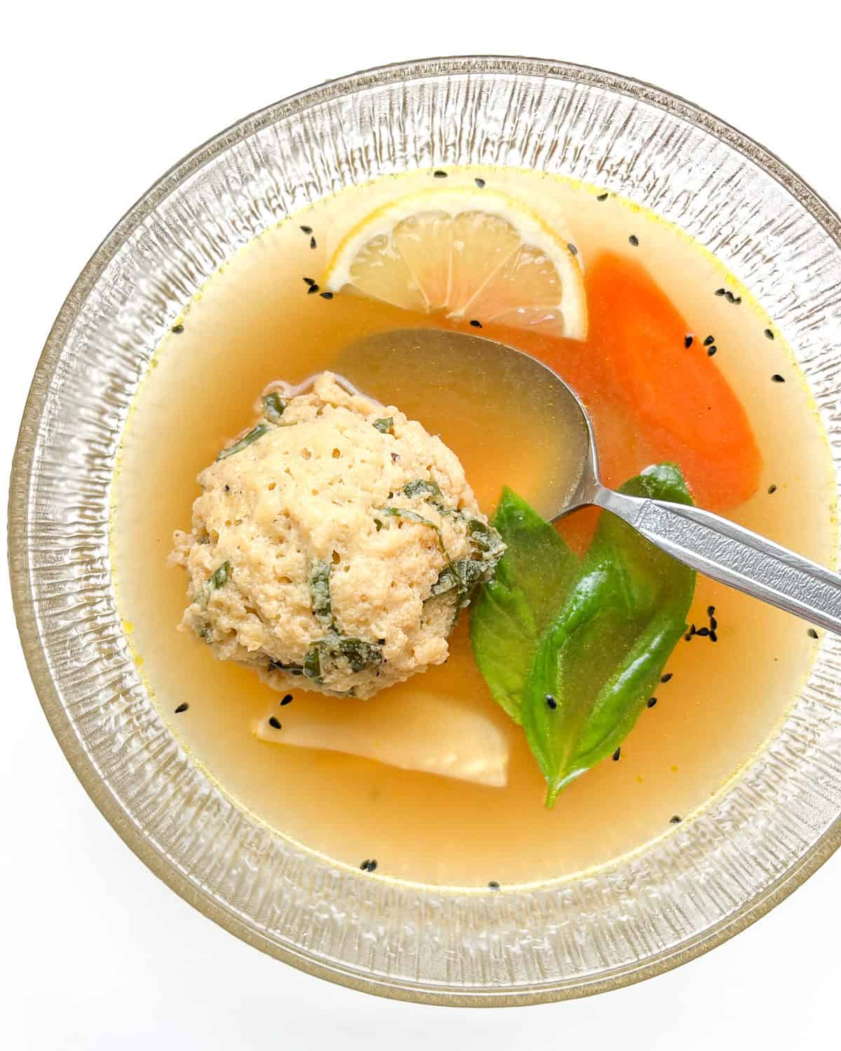 A serving of the matzo ball soup in a clear glass bowl.