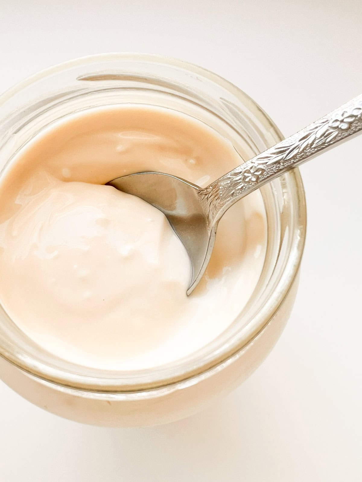A close up image of a jar of baked milk yogurt with a floral patterned silver spoon scooping some of the yogurt.
